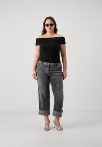 Μαύρο οφ-σόλντερ κορμάκι με ραμμένο ύφασμα, συνδυασμένο με γκρι τζιν με ρολό στην άκρη και ασημένιες κορδονάτες γόβες. Το μοντέλο φοράει σκούρα γυαλιά ηλίου.