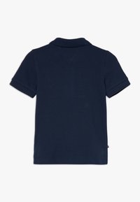 Námořnická modrá polokošile s krátkými rukávy, plochým límcem, žebrovanými manžetami a strukturovanou tkaninou. Obsahuje malé logo na lemu.
