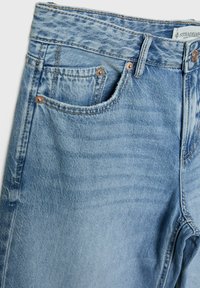 Helleblaue Jeans aus Denim mit strukturiertem Finish, ausgestattet mit einem Fünf-Taschen-Design und kupferfarbenen Nieten. Der Bund zeigt das Markenlabel.