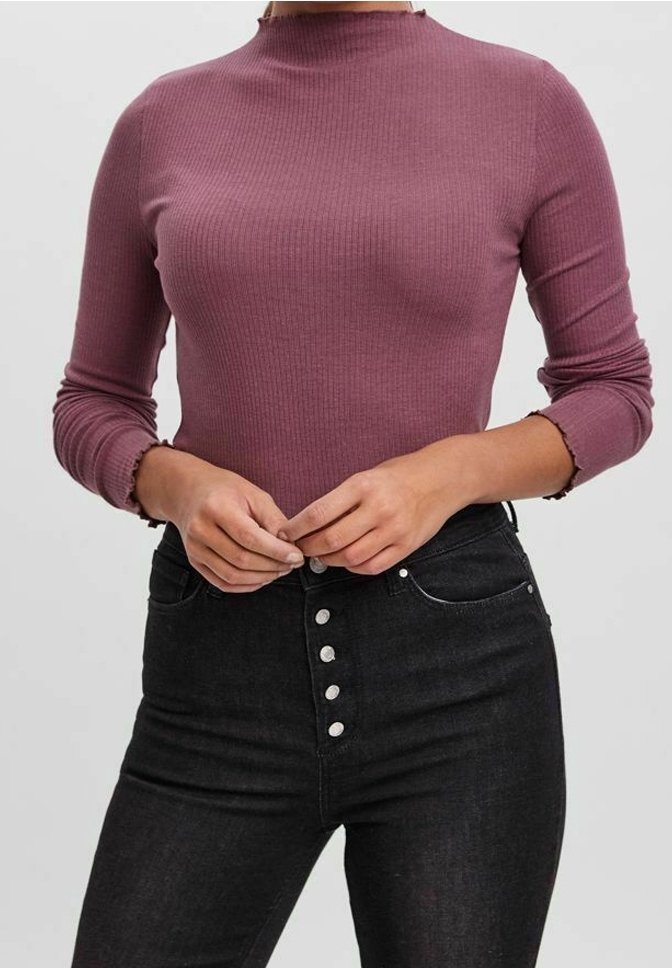 Rippstrick-Oberteil mit langen Ärmeln in Mauve, mit hohem Kragen und gewellten Bündchen, kombiniert mit hochTaillierten schwarzen Jeans mit silbernen Knöpfen.