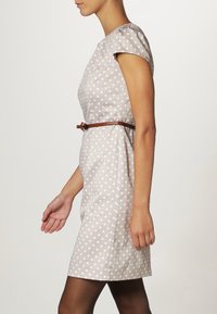 Abito beige a pois con maniche a cappuccio, un corpetto aderente e una cintura marrone in vita, caratterizzato da una texture liscia e un design che arriva fino al ginocchio.