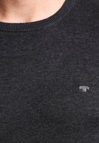 Dark gray knit sweater with a ribbed texture and a round neckline. Small logo in a lighter gray on the lower left side.