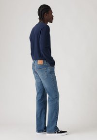 Camisa de manga larga de color navy combinada con jeans rectos de color azul claro. Los jeans cuentan con un parche de cuero en la parte trasera y detalles de costura sutiles.