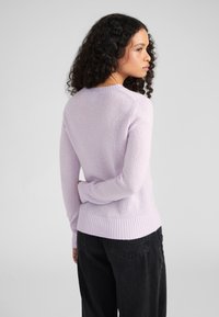 Lila Rundhals-Pullover aus weichem Strickstoff mit gerippten Bündchen und Saum. Trägt man mit lockeren schwarzen Hosen, von hinten betrachtet.