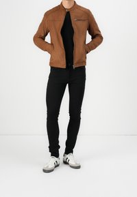 Bruin faux suede jack met een staande kraag, ritsluiting en zijzakken. Gecombineerd met zwarte skinny jeans en witte sneakers.
