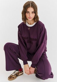Fialová mikina a odpovídající kalhoty s texturovaným designem "Jednou dávno"; spárováno s teniskami s leopardím potiskem a červenými ponožkami.