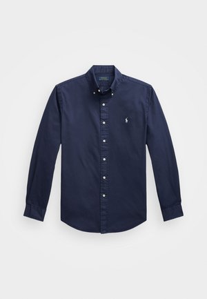 Camisa azul marinho de manga longa com botão, feita de algodón, apresentando um pequeno logótipo bordado no peito e botões brancos na parte da frente.