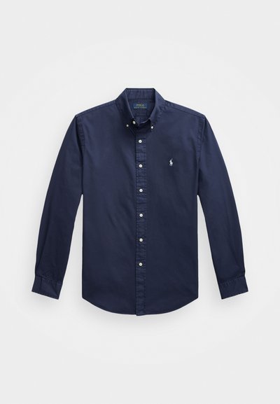 Βαθύ μπλε πουκάμισο μακρυμάνικο με κουμπιά, φτιαγμένο από βαμβάκι, με μικρό κεντητό λογότυπο στο στήθος και λευκά κουμπιά στο μπροστινό μέρος.