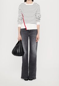 Pull rayé blanc avec un accent rouge, associé à un jean évasé gris. Le mannequin tient un sac à main noir texturé. Design simple et moderne.