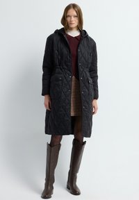 Czarna pikowana kurtka z kapturem, dwoma przednimi kieszeniami i zapięciem na napy. Noszona na bordowym swetrze i wzorzystej spódnicy z długimi brązowymi botkami.