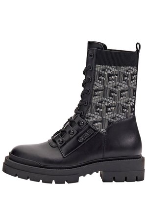 Botte de combat noire en cuir et tricot avec semelle épaisse, laçage à l'avant, panneau en tissu texturé avec motif géométrique et nom de la marque "GUESS" sur le côté.