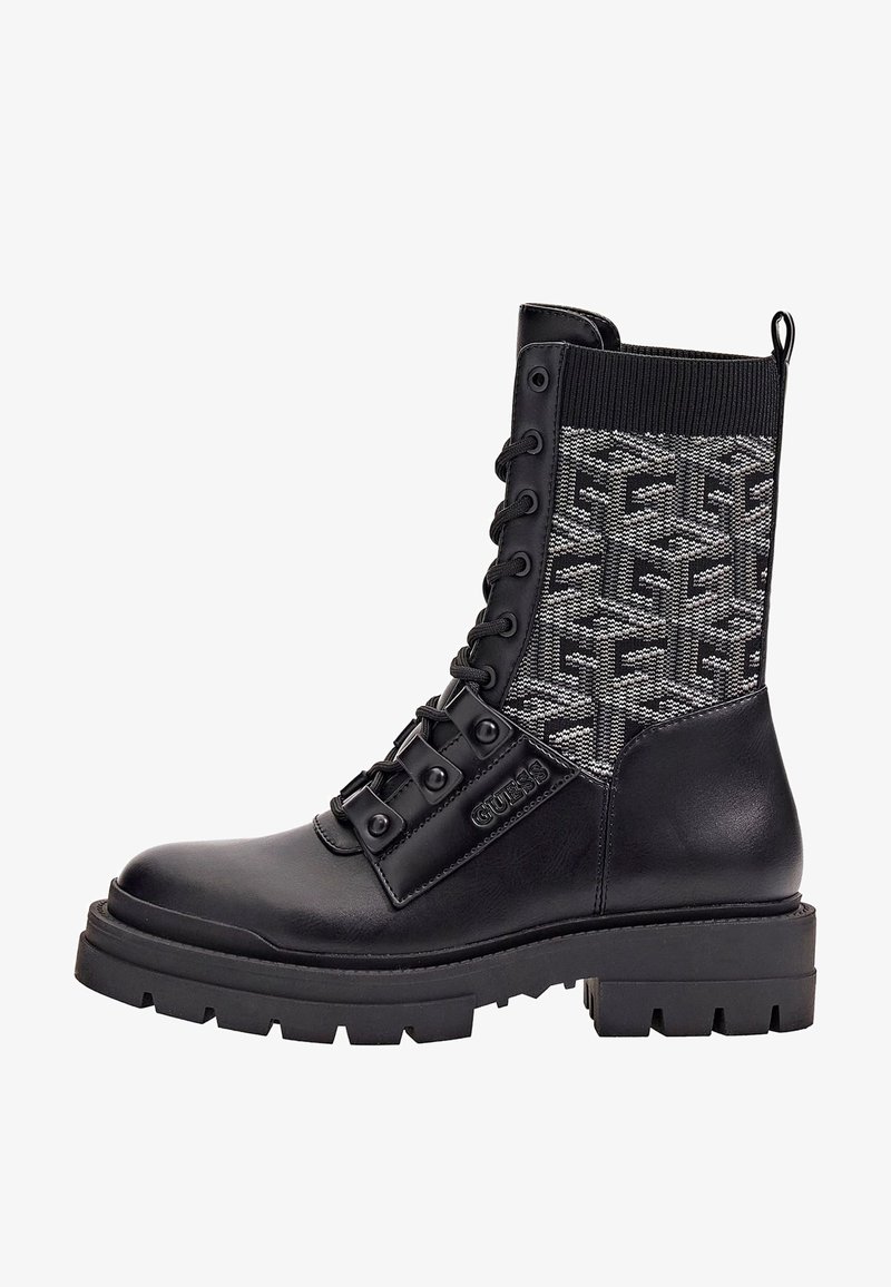 Botte de combat noire en cuir et tricot avec semelle épaisse, laçage à l'avant, panneau en tissu texturé avec motif géométrique et nom de la marque "GUESS" sur le côté.