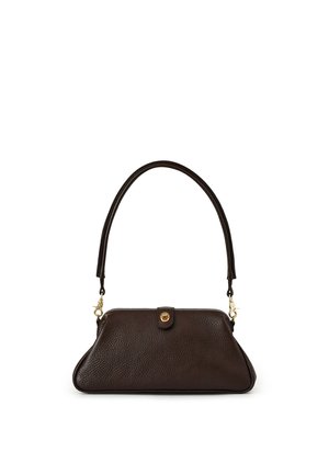 Mujer con pelo rizado sonríe, lleva una chaqueta vaquera oscura y porta un bolso marrón texturizado al hombro sobre un fondo neutro.