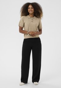 Beige, rövid ujjú póló pulóver, gallérral és három gombbal, laza szabású fekete nadrággal és világos színű cipővel párosítva.