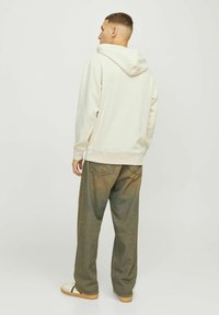 Jasno beżowy hoodie o luźnym kroju, z kapturem, długimi rękawami i ściągaczem u dołu, w zestawie z wyblakłymi zielonymi spodniami o szerokich nogawkach.