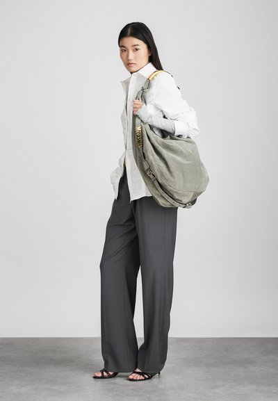 Harmaa mokkaville olkalaukku, jossa on rento muotoilu, kullanväriset yksityiskohdat ja teksturoitu hihna, jota kantaa malli löysissä harmaissa housuissa.