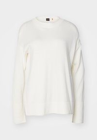 Maglione bianco lavorato a maglia con scollo rotondo, spalle basse e bordo a coste. Il tessuto è liscio, con una leggera luminosità. Etichetta del marchio visibile.