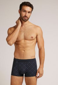 Černé boxerky ve stylu trunk s modrým hvězdicovým vzorem, vyrobené z měkké látky s klasickým pasem a přiléhavým střihem pro pohodlí.
