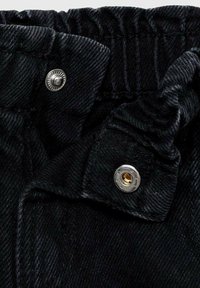 Tessuto di denim nero con una finitura texture, caratterizzato da una cintura elastica e dettagli in metallo argentato con un inserto dorato.