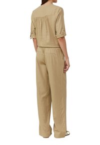 Lichtbeige linnen jumpsuit met korte mouwen, detail met plooi aan de achterkant, elastische tailleband en zijzakken; ontspannen pasvorm met broekspijpen tot op de grond.