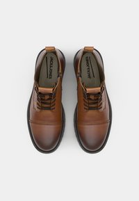 Zapatos de cuero marrón con punta redonda, superficie texturizada y suelas de goma negra. Presentan un diseño con cordones y una pequeña lengüeta en el talón.