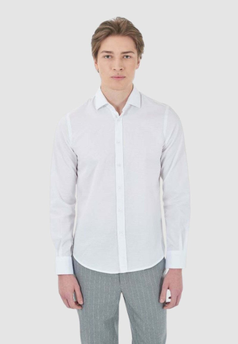 Camicia bianca a maniche lunghe con bottoni, caratterizzata da una texture sottile, con colletto e polsini classici, abbinata a pantaloni grigi a righe sottili.