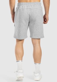 Pantalones cortos de algodón gris con una cintura elástica, bolsillos laterales y un pequeño detalle de logo. La tela tiene una textura suave y lisa.