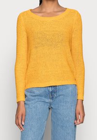 Pull en tricot jaune avec un décolleté arrondi large, des manches longues et une coupe décontractée. Tissu léger et texturé avec des poignets côtelés.