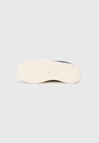 Black sneaker with a textured upper, featuring a white rubber sole. Tread pattern on sole for grip, no visible branding. Simple design.
