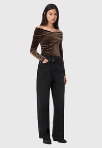 Brun velour-top med bare skuldre kombineret med højtaljede sorte bukser med vide ben. Bukserne har forlommer og knaplukning.