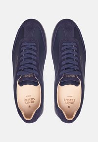 Marineblaue Sneaker aus einer Kombination von Wildleder und glattem Material, mit flachen Schnürsenkeln, einem gepolsterten Kragen und einem minimalistischen Design.