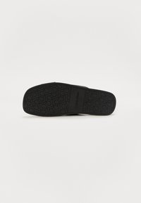 Svart sandaler med en teksturert gummisåle med et gjentatt logo-mønster, flat form og bred stroppdesign.