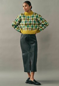 Strikket gul-grønternet sweater med høj hals, parret med en fitted sort lædernederdel med en slids foran og en slank silhuet.