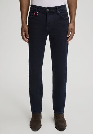 Granatowe dżinsy o slim fit, z czerwonym akcentem w postaci pierścienia na szlufce paska oraz subtelnie wystrzępioną teksturą.