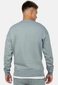 Felpa grigia chiara con una vestibilità comoda, polsini e orlo a coste, e una texture liscia; la vista posteriore mostra un design con scollatura a girocollo.