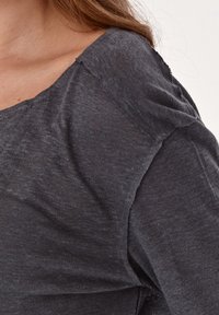 Top ligero de color gris oscuro con un ajuste holgado, cuello amplio y textura sutil. La tela parece suave con una ligera transparencia en los bordes.