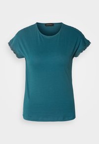 Haut pour femme à manches courtes de couleur sarcelle avec bordure en dentelle sur les manches et encolure ronde, présenté sur un fond clair uni.