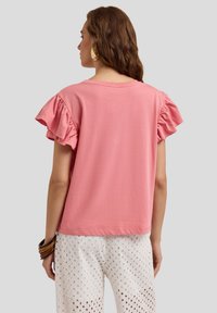 T-shirt rose à manches courtes avec des manches volantes, coupe décontractée et texture douce. Porté avec un pantalon brodé blanc.