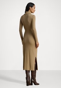 Woman wearing a fitted, long-sleeve, camel-colored midi dress with a side slit, paired with knee-high dark brown heeled boots.