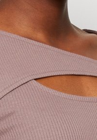 Ribbad lila topp med bred axelrem och en utskärning vid halslinningen. Närbilden fokuserar på struktur och design.