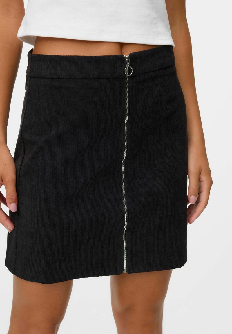 Zwarte corduroy rok met een voorkant rits en metalen hardware. Heeft een rechte snit en een gestructureerde stof, met een lengte tot halverwege de dij.