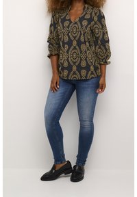 Svart blus med guldig geometrisk mönster, V-ringat, puffärmar. Kombinerad med åtsittande blå jeans och svarta loafers. En enkel design med subtil textur.