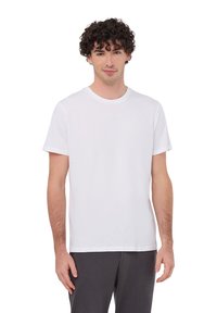 Biała koszulka z krótkim rękawem, wykonana z bawełny, z okrągłym dekoltem i luźnym krojem, noszona z szarymi spodniami. Prosty i uniwersalny design.