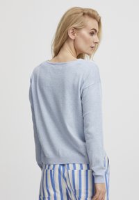 Pullover azzurro chiaro con una vestibilità comoda, maniche lunghe, collo rotondo e orlo a costine. Indossato sopra pantaloni a righe blu e bianchi.