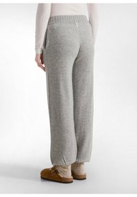 Grijze gebreide sweatpants met een ribbelachtige tailleband, voorzien van zijzakken en een relaxed fit, gecombineerd met bruine klompen en gemêleerde sokken.