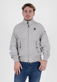 Giacca bomber grigia chiara con colletto alto, chiusura con zip, due tasche laterali, polsini elasticizzati e un sottile marchio sulla spalla.