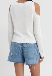 Biały dziany sweter z odkrytymi ramionami, prążkowanym dekoltem i mankietami. W zestawie niebieskie szorty dżinsowe z postrzępionym dołem i tylnymi kieszeniami.