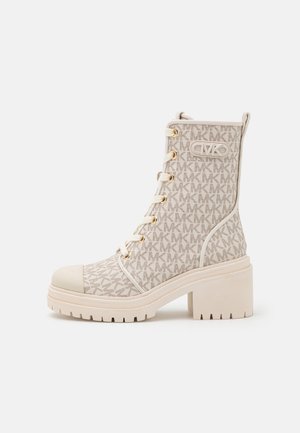 Botte de combat à talons hauts beige avec motif monogramme MK, devant lacé avec œillets dorés, semelle en caoutchouc et logo Michael Kors à la cheville.