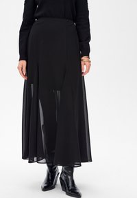 Zwarte, vloerlange rok van lichtgewicht, doorschijnende stof met een effenvoering. Beschikt over een gladde tailleband en subtiele plooien.