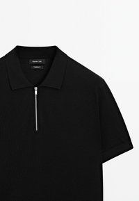 Černé polo tričko s krátkým rukávem vyrobené z jemné vlny, s límečkem na zip a hladkým, texturovaným povrchem. Jednoduchý design bez viditelných vzorů.